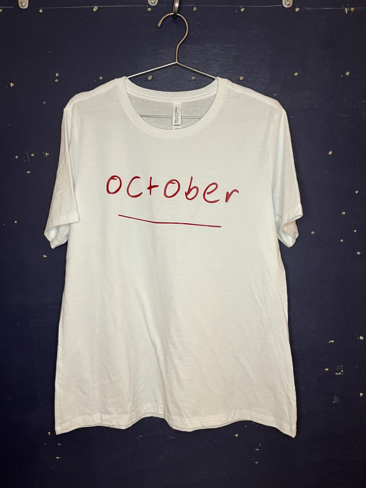 White t-shirt with 'October' printed on it hanging against a dark background